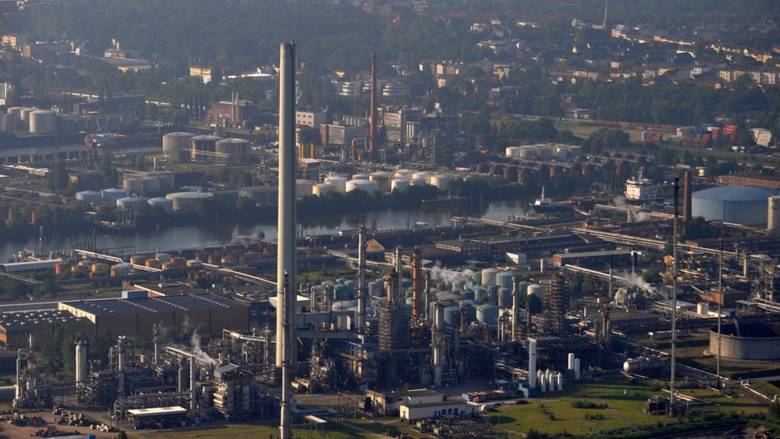 Luftbild auf eine im Dunst liegende Industrielandschaft mit vielen Öltanks und Schloten.