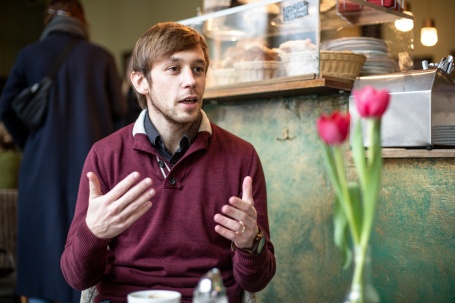 Ein junger Mann in einem Kaffe im Gespräch, gestikulierend.