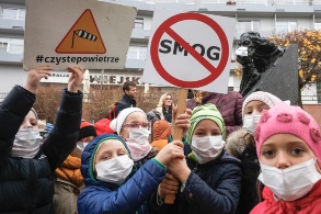 Kinder vor einem Wohnhaus demonstrieren mit Schildern und Atemmasken.
