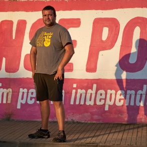 Ein Mann im T-Shirt steht vor einer Mauer, auf der ein Slogan aufgemalt ist.