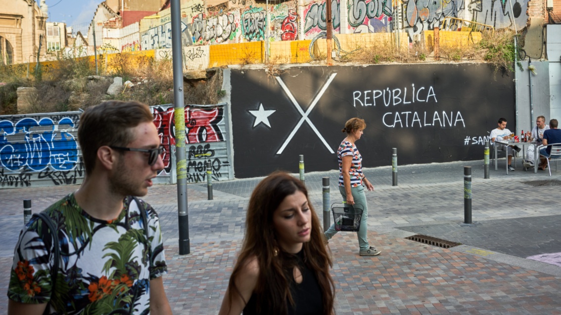 Zwei junge Menschen laufen vor einem schwarzen Transparent, auf dem ein großes X steht.