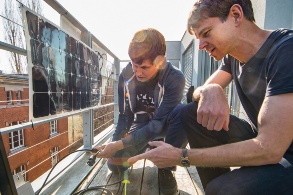 Zwei junge Männer bei der Montage eines Solarmoduls auf einem Balkon