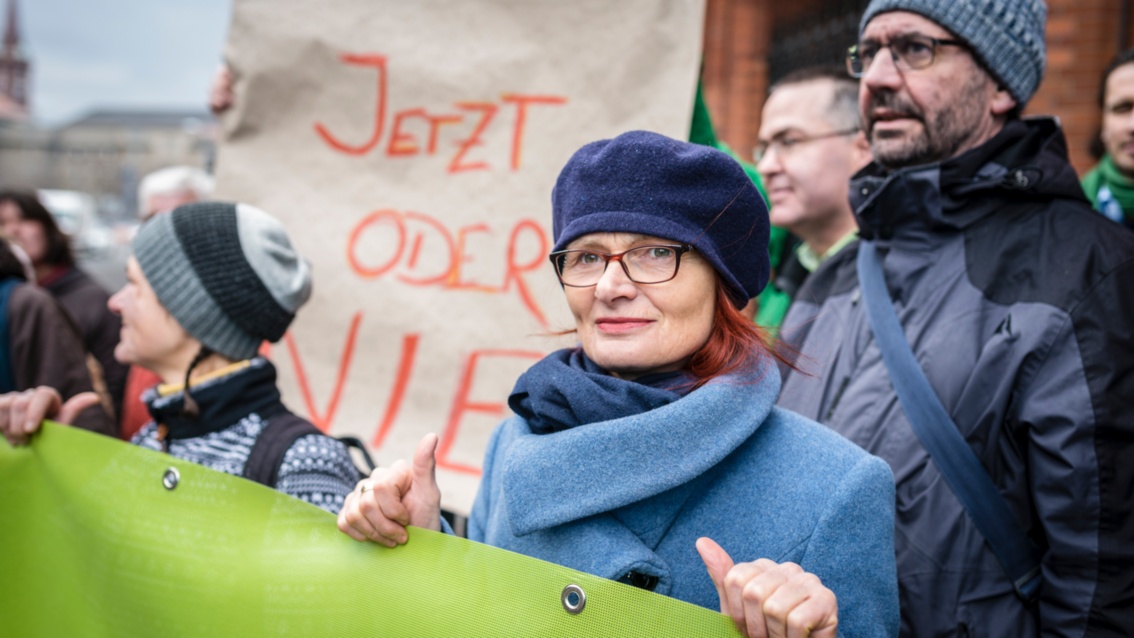 Demonstranten mit Transparenten, in Nahaufnahme eine Frau in winterlicher Kleidung
