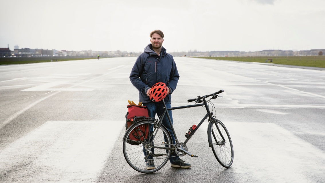 Junger Mann steht mit seinem Fahrrad auf dem weiten Tempelhofer Feld