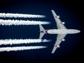 Man sieht ein Flugzeug am Himmel, das vier Kondensstreifen hinter sich lässt