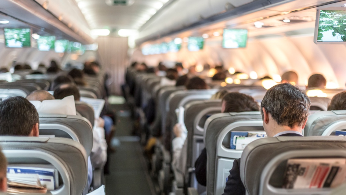 Gang in einem Flugzeug, die sitzenden Passagiere, hauptsächlich Geschäftsreisende, sind von hinten zu sehen.