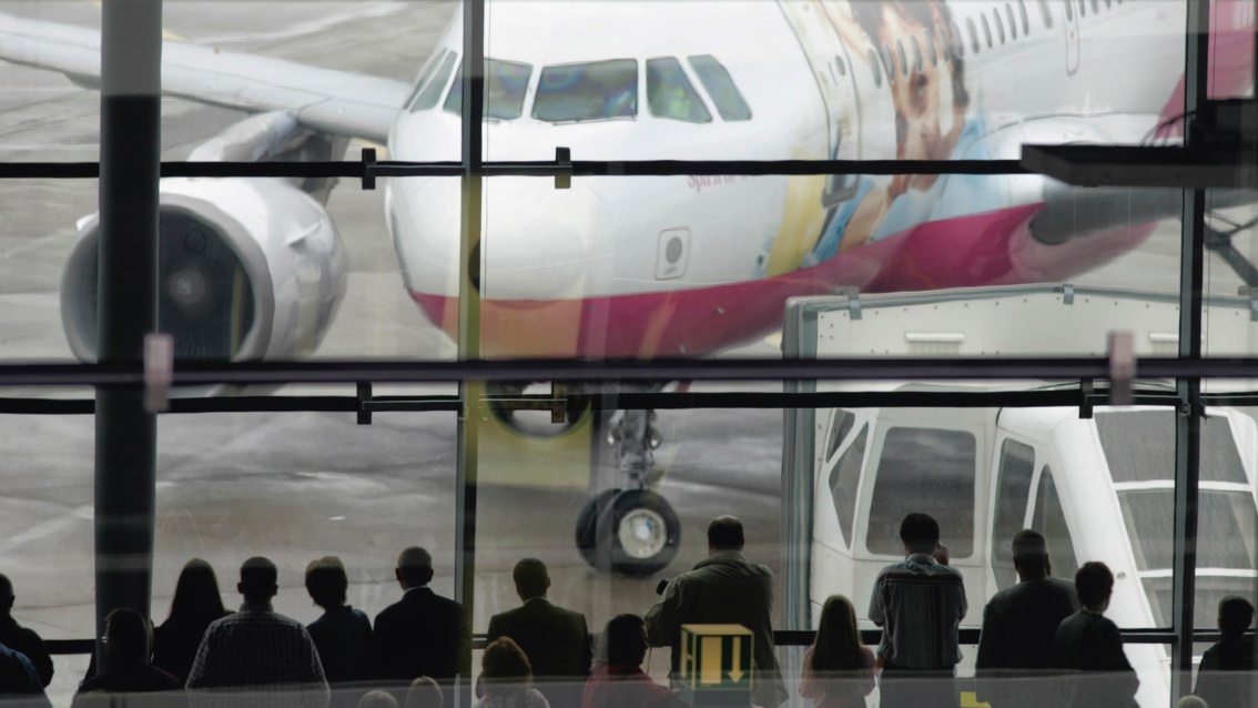Vor einem Fenster stehen Menschen und schauen auf die Schnauze eines Passagierflugzeuges.