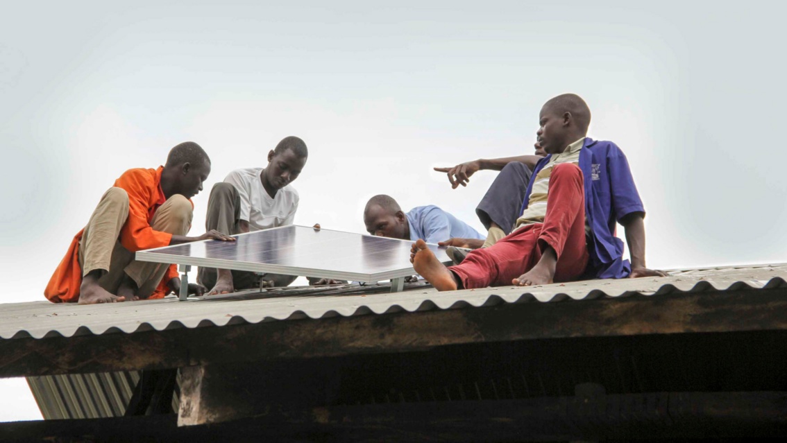 Vier afrikanische Männer auf einem Dach beim Installieren einer PV-Anlage