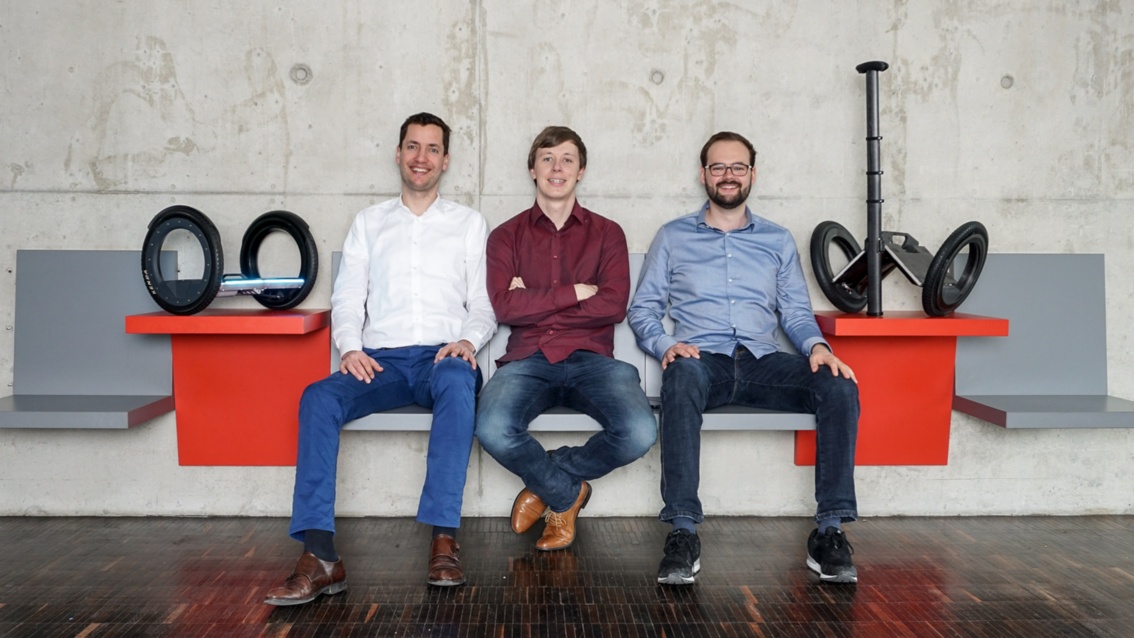Drei Unternehmensgründer sitzen beisammen, daneben die von ihnen entwickelten E-Floater.