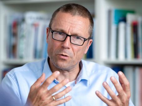 Brustportrait eines Mannes mit Brille und Hemd, der erläuternd die Hände hebt