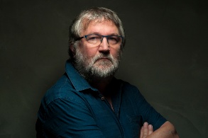 Ernst dreinblickender grauhaariger Mann mit Bart und Brille