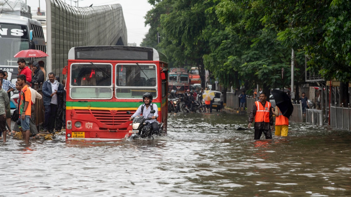Eine überflutete Straße, ein Bus steht, Fußgänger waten durch das etwa ein Meter tiefe Wasser.