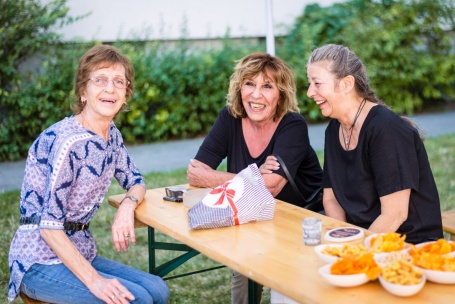 Drei Frauen sitzen an einem Biertisch im Grünen und amüsieren sich.