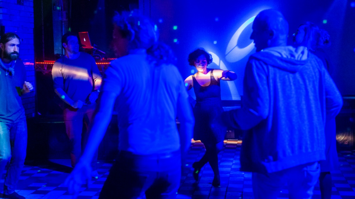 Eine tiefblau beleuchtete Tanzfläche mit ein paar Tänzern.