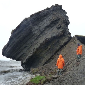 Forscher betrachten einen Felsbrocken an einer Küste, der ins Wasser zu fallen droht.