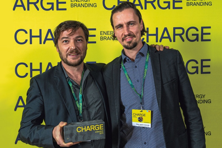 Zwei junge Männer vor einer gelben Wand mit der Beschriftung «Charge» lachen in die Kamera.