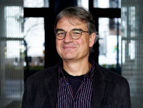 Mann mit grauen Haaren und Brille vor einer blauen Wand