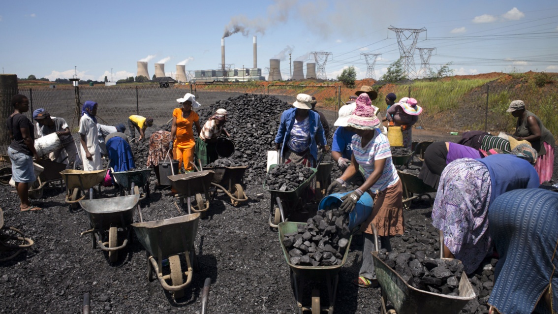 Vor einem Kohlekraftwerk füllen Menschen Kohle in ihre Schubkarren.
