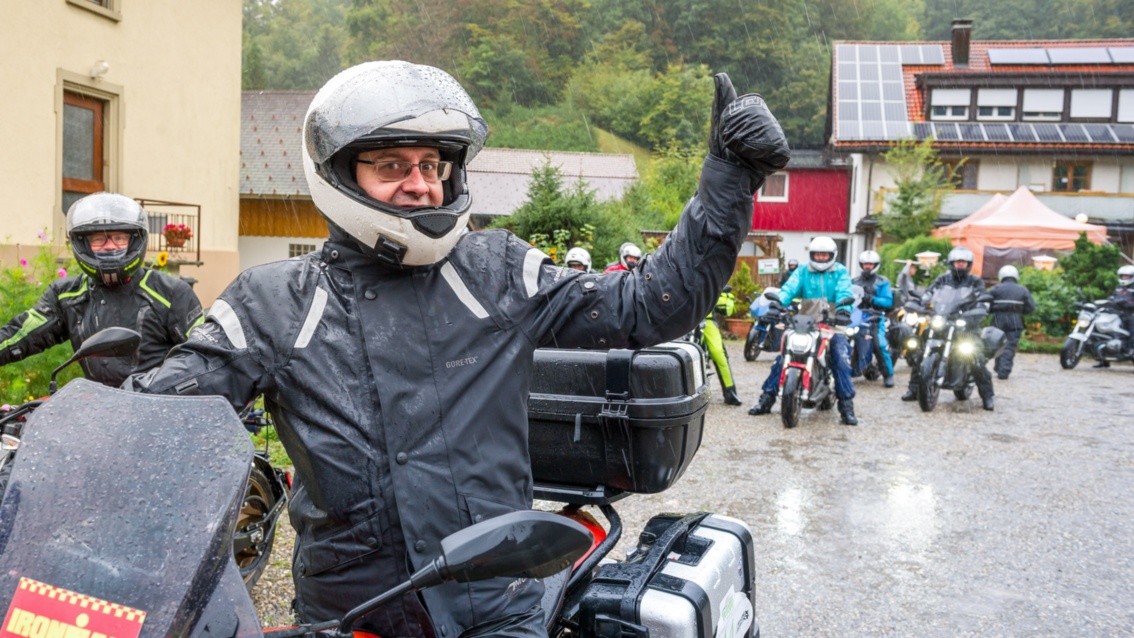 Eine Gruppe von Motorrädern im Regen, im Vordergrund hebt ein Mann den Daumen, zum Start der Kolonne.