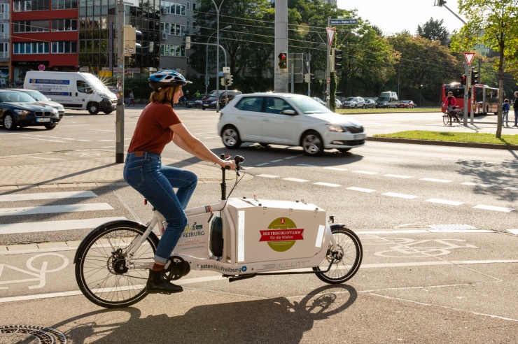 Eine junge Frau ist mit einem Lastenrad im Stadtverkehr unterwegs.