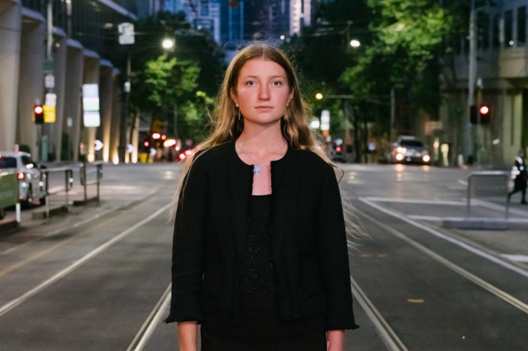 Eine junge Frau steht selbtbewusst in der Mitte der Straße im nächtliche Melbourne.