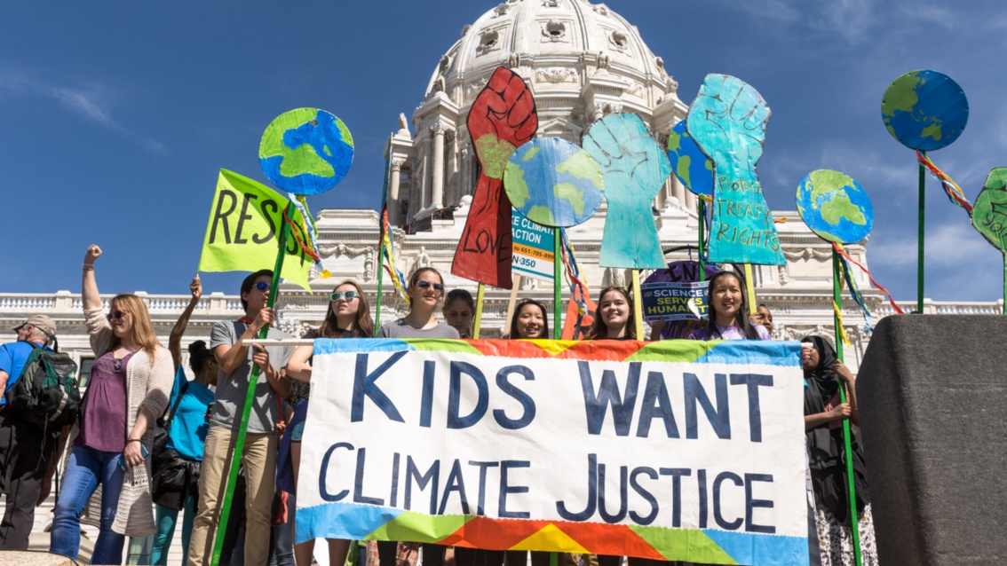 Eine Gruppe junger Menschen demonstriert vor einer weißen Kirche. Auf ihrem Transparent steht: "Kids want Climate Justice".
