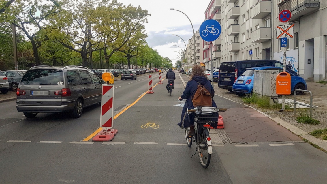 Auf einer mehrspurigen Straße ist mit Barken und gelben Markierungen eine Fahrspur für Radfahrer gekennzeichnet.