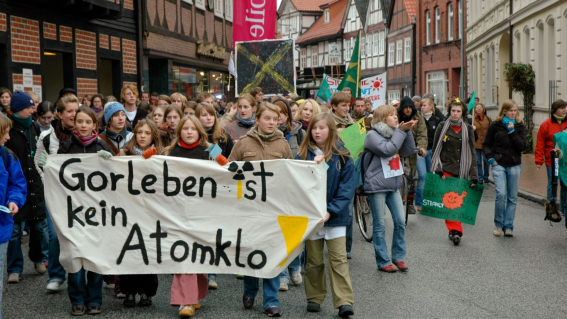 Eine Gruppe von Schülerinnen und Schülern zieht durch eine von Fachwerkhäusern gesäumte Straße, voran ein Banner mit der Aufschrift «Gorleben ist kein Atomklo!»