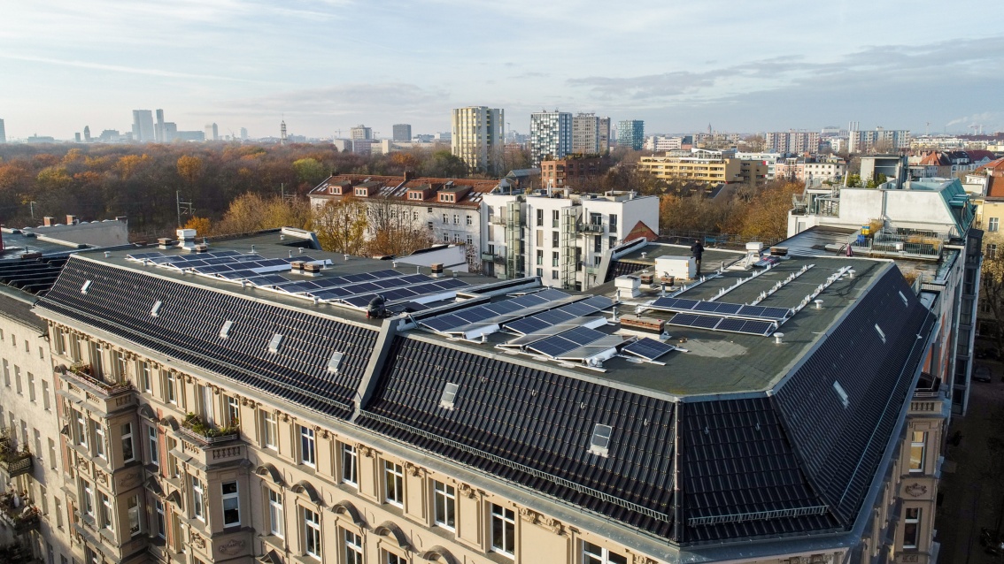 Blick über Berlin, im Vordergrund die große Dachfläche eines Gründerzeithauses, auf dem PV installiert wird.