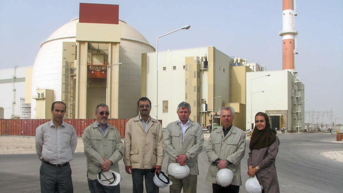 Ein Gruppe von fünf Männern und einer Frau posiert vor einem Kraftwerksbau. Alle halten Bauhelme in der Hand.