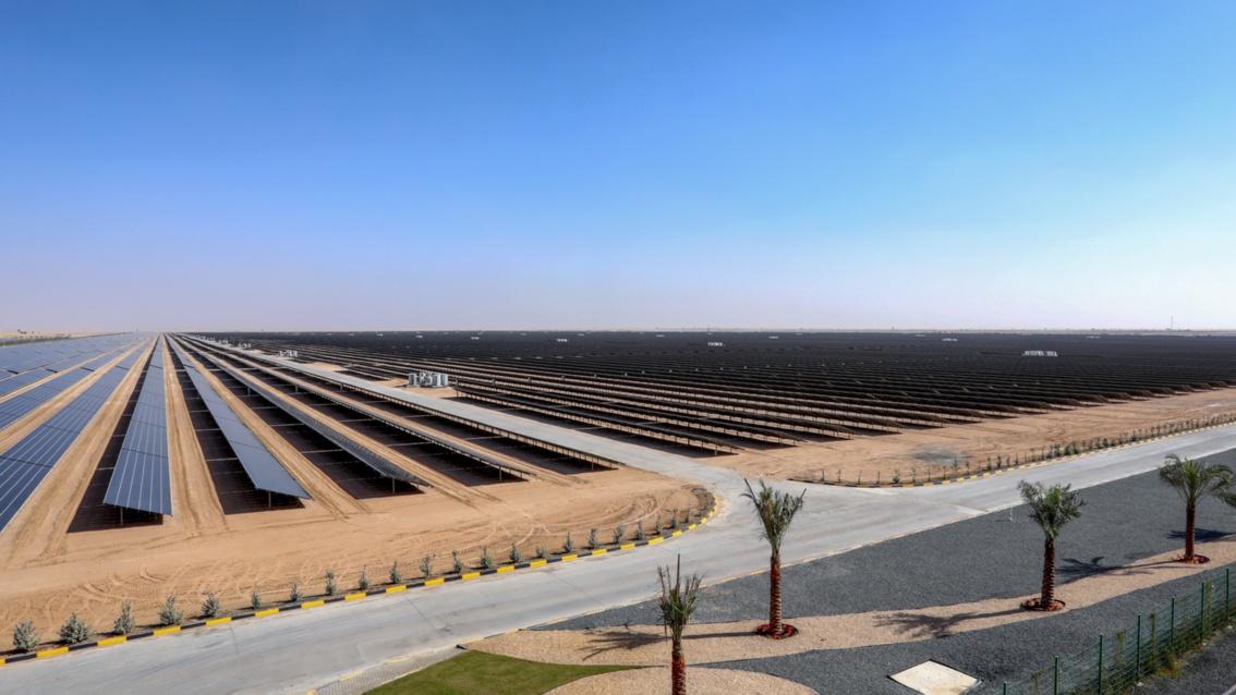 Endlos erscheinende Reihen von Solarmodulen auf einer eingezäunten Freifläche in einer flachen kargen Landschaft