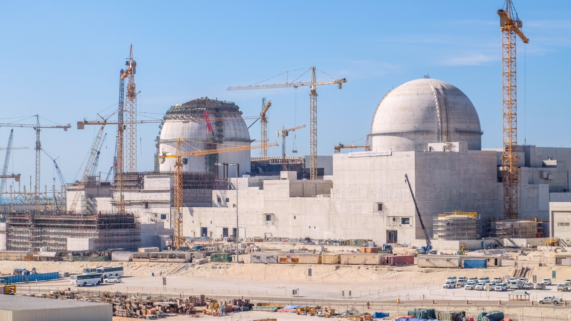 Eine Großbaustelle mit zwei charakteristischen runden Reaktorkuppeln und zahlreichen Baukränen in gleißender Sonne