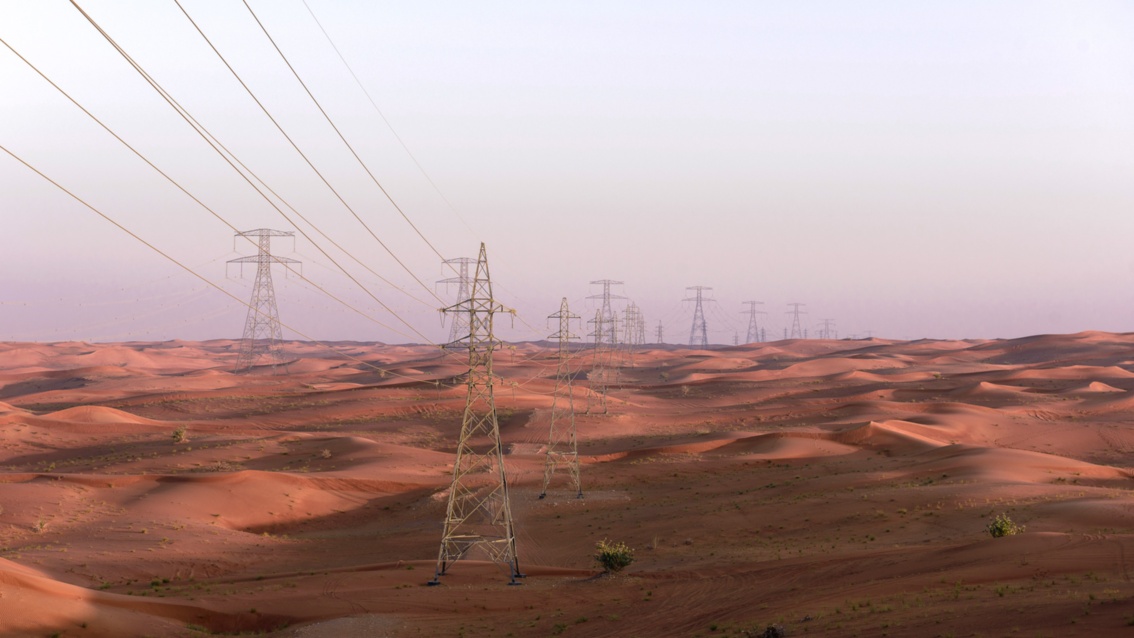 Durch eine Wüste aus rotem Sand ziehen sich zahlreiche Hochpannungsleitungen bis zum Horizont.