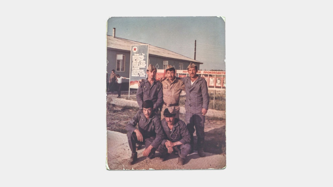 Ein altes Farbfoto mit ausgefranstem Rand zeigt eine Gruppe von fünf jungen Männern in Arbeitsuniformen.