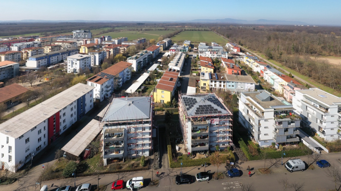 Luftaufnahme eines Stadtviertels, auf den Dächern im Vordergrund sind PV Anlagen zu sehen, im Hintergrund der Schwarzwald.