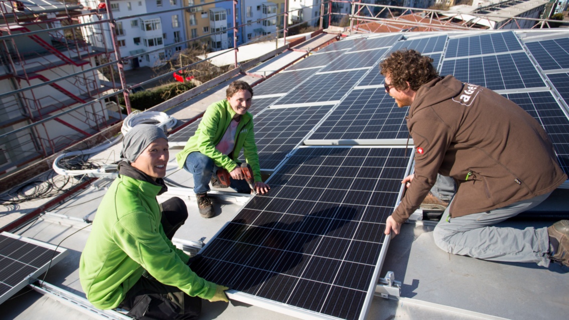 Auf einem Dach werden von drei Personen Solarpanele installiert.