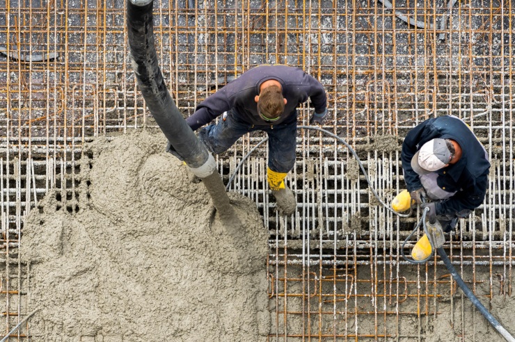 Ansicht von oben: Beton wird über Stahlmatten gegossen, zwei Bauarbeiter stehen dabei.