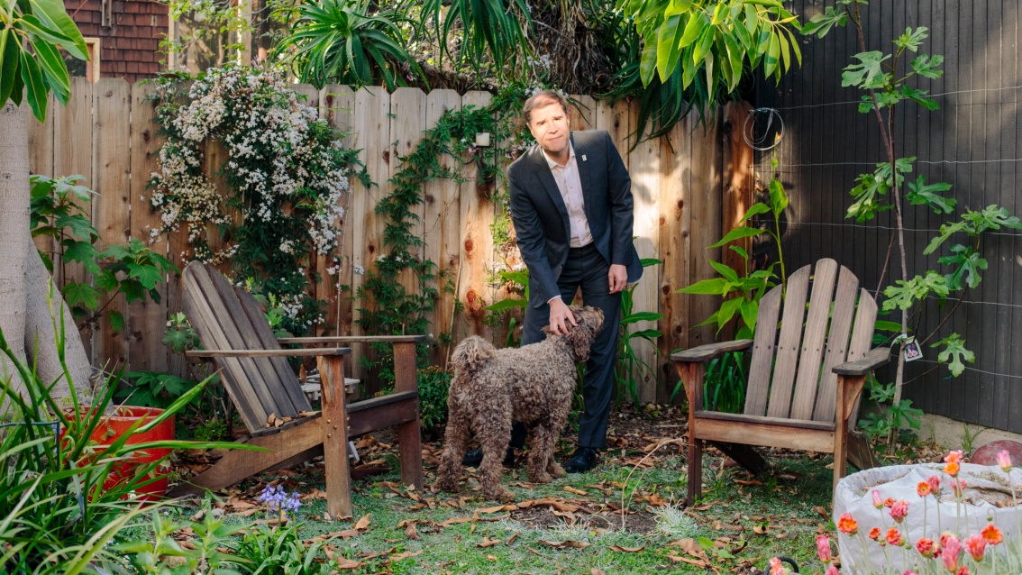 Wackernagel steht in seinem Garten und streichelt seinen Hund.