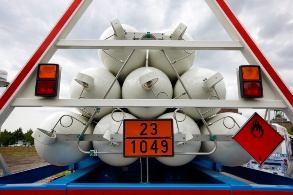 Acht Wasserstofftanks liegen, von einer Stahlkonstruktion gesichert, auf einem Autoanhänger. 