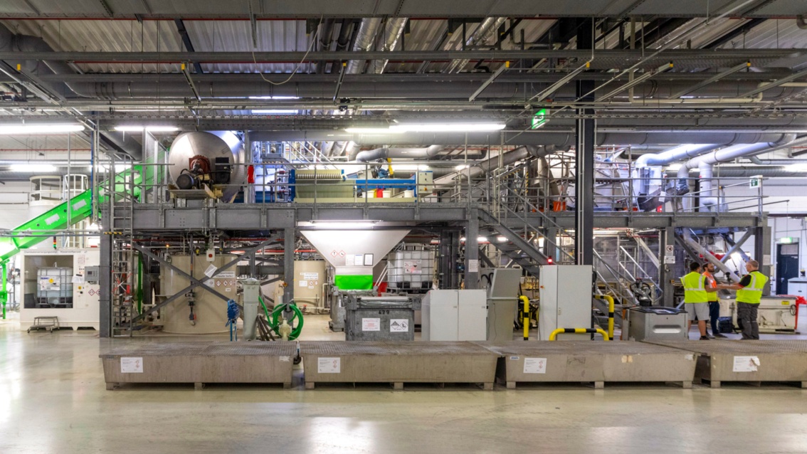 In einer Industriehalle steht eine große Maschine mit mehreren Ebenen und Wartungstreppen.