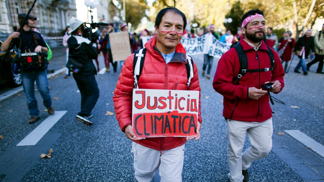 Zwei junge Männer auf einer Demo. Auf dem Transparent, das einer von ihnen trägt, steht auf Spanisch «Klimagerechtigkeit»