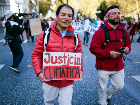 Zwei junge Männer auf einer Demo. Auf dem Transparent, das einer von ihnen trägt, steht auf Spanisch «Klimagerechtigkeit»