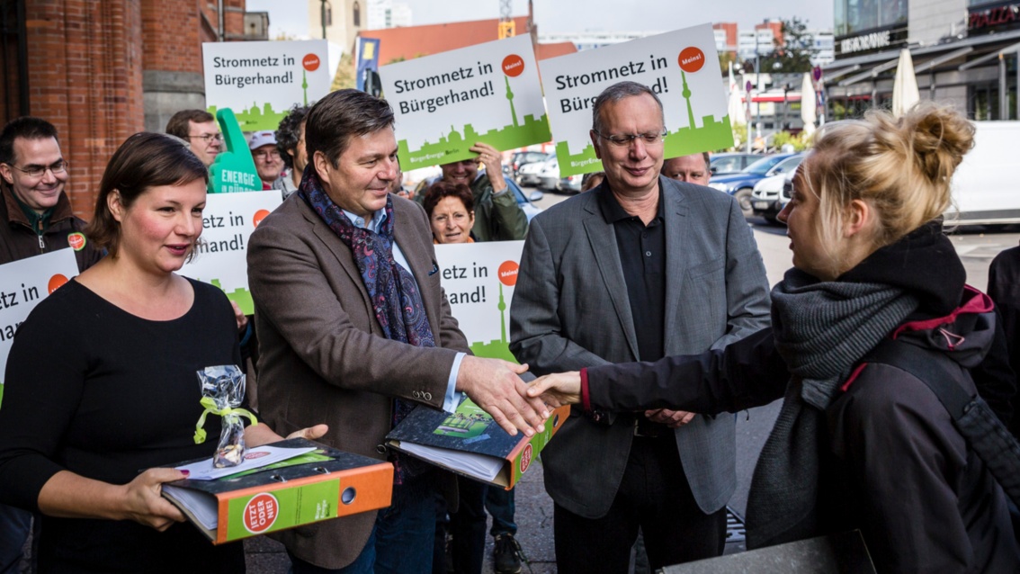 Vor dem Roten Rathaus in Berlin hat sich eine Gruppe mit Transparenten versammelt. Im Vordergrund stehen drei Politiker, einer schüttelt die Hand einer jungen Frau.
