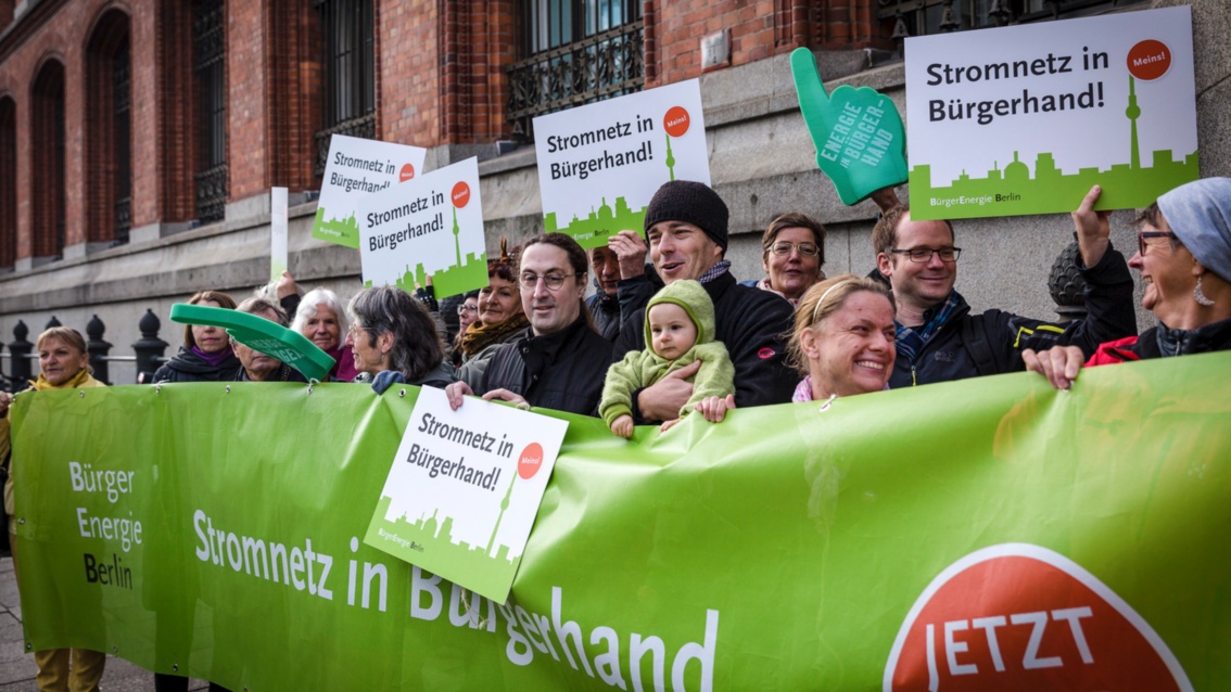 Some 20 people stand behind a green banner in front of Berlin’s Rotes Rathaus with signs in their hands.