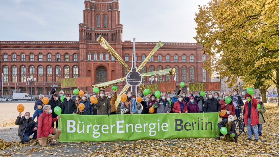 Some 40 people  are lined up for a group photo in front of Berlin’s Rotes Rathaus at an information stand, holding a cardboard TV Tower that radiates golden sunbeams.