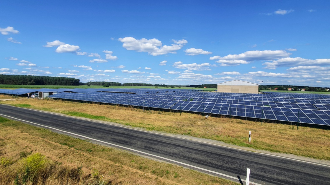 A solar farm of PV modules runs alongside a country road.
