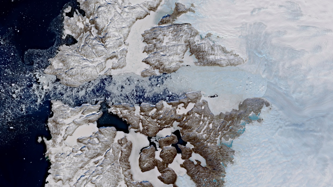 Ein Bild aus dem All zeigt links den dunklen Ozean, von Schnee überstäubte braune zerklüftete Landmasse und rechts Schneeflächen.