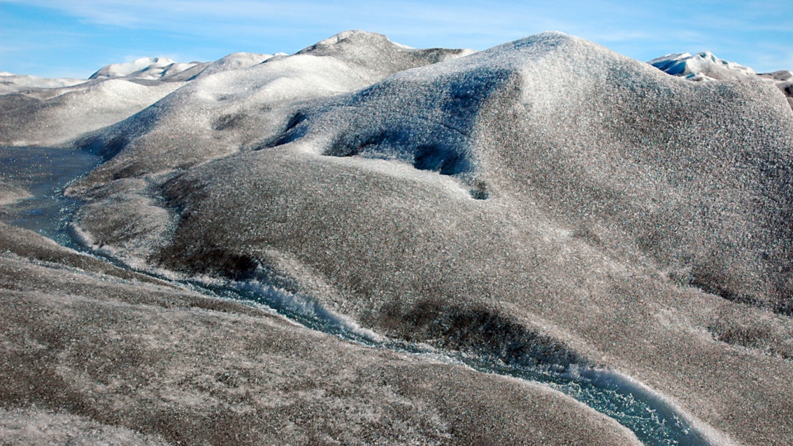 Durch graubraun gefärbte Eishügel fließt klares blaues Wasser in Schluchten hinab.