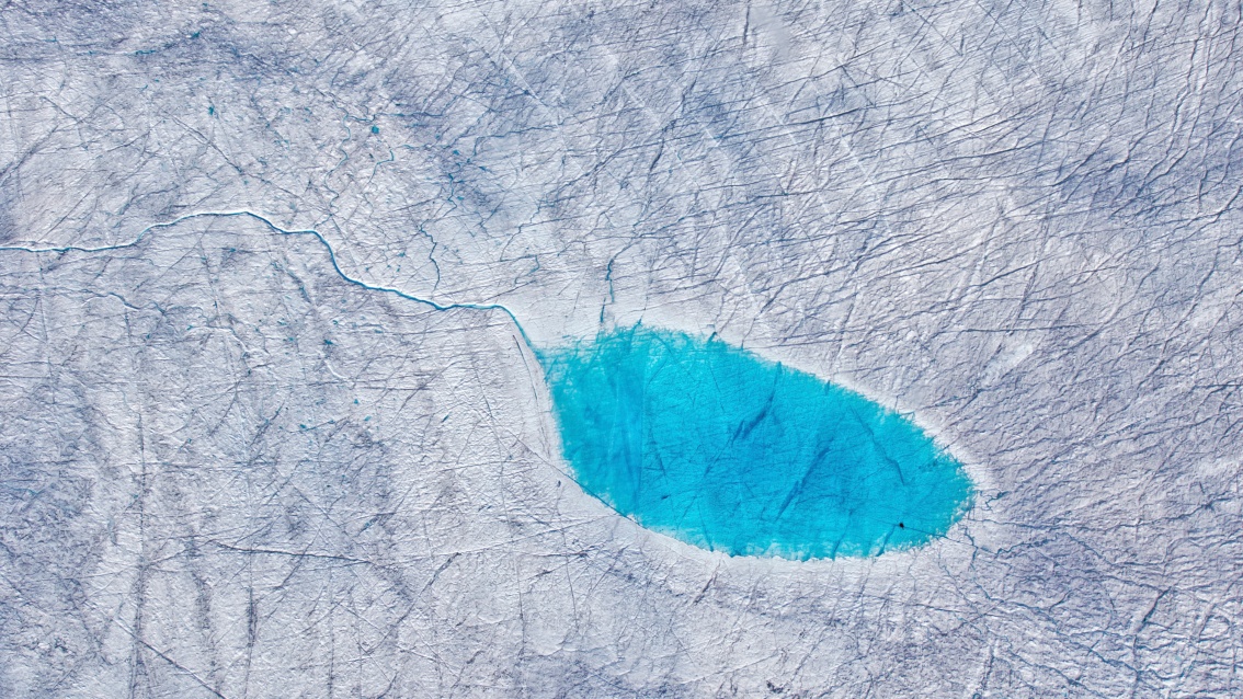 Auf einer weißen zerfurchten Flächemündet ein kleiner Fluss in einen aquamarinblauen See.