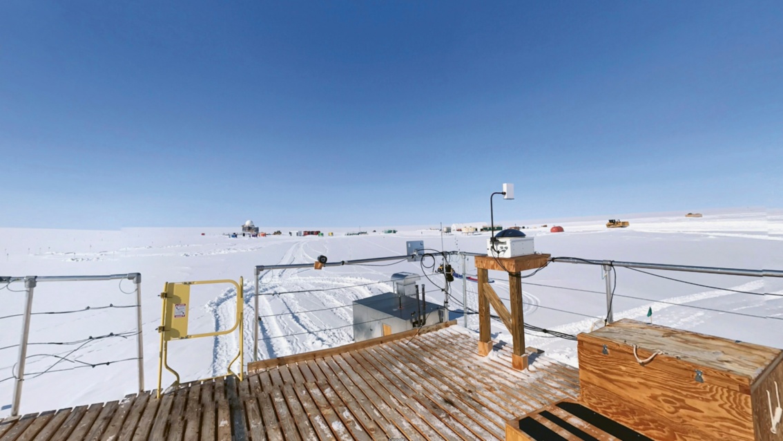 Ein Panoramabild von einer Holzrampe aus fotografiert, zeigt eine weite Schneefläche auf der eine Reihe flacher Gebäude stehen.